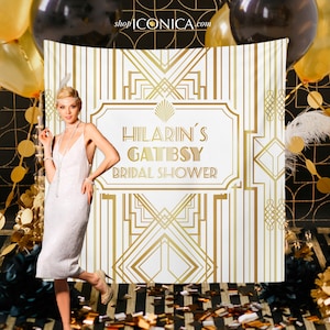 May include: A white backdrop with a gold art deco design and the text "Hilarin's Gatsby Bridal Shower". A woman in a white flapper dress stands in front of the backdrop.