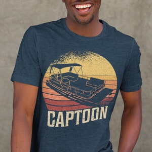 May include: A navy blue t-shirt with a vintage-style graphic of a pontoon boat in a sunset. The text "CAPTOON" is printed below the graphic.