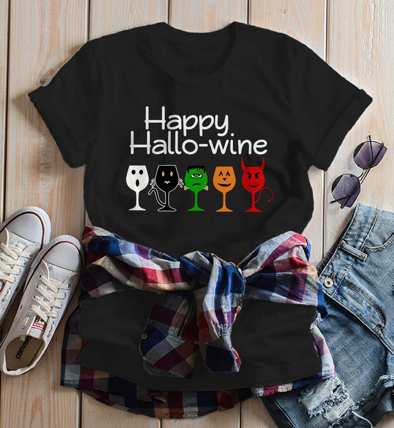 K&ouml;nnte beinhalten: Schwarzes T-Shirt mit dem Text "Happy Hallo-wine" und einer Reihe von f&uuml;nf Weingl&auml;sern mit verschiedenen Halloween-Charaktergesichtern.