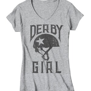 May include: Gray V-neck t-shirt with a distressed black graphic of a roller derby helmet with a star and the text "Derby Girl".