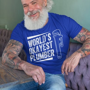 May include: A blue t-shirt with a white graphic that says "WORLD'S OKAYEST PLUMBER" and a wrench illustration.