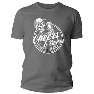 May include: A grey t-shirt with a white graphic. The graphic shows a skeleton wearing a cap and holding a beer mug, with the words "Cheers & Beers To My 30 Years" in a circular design.