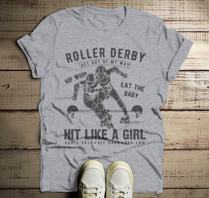 May include: Gray t-shirt with a roller derby graphic. The graphic features two roller derby players skating and the text "Roller Derby Get Out Of My Way Hip Whip Eat The Baby Hit Like A Girl Skate Fast Hit Hard Get Low".