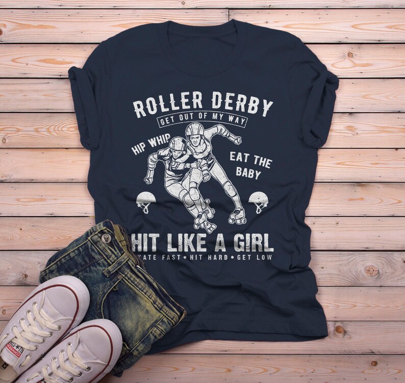 May include: A navy blue t-shirt with a white graphic of two roller derby players. The text on the shirt reads "Roller Derby Get Out of My Way Hip Whip Eat the Baby Hit Like a Girl Skate Fast Hit Hard Get Low".