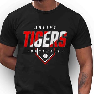 May include: Black t-shirt with the text "JOLIET TIGERS BASEBALL" in red and white. The design includes a baseball diamond graphic with a baseball. The shirt is short-sleeved.