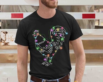 May include: Black t-shirt featuring a white outline of a rooster decorated with colorful Christmas lights. The shirt is worn with blue jeans, a brown belt, and yellow work gloves. A white cowboy hat is also worn.