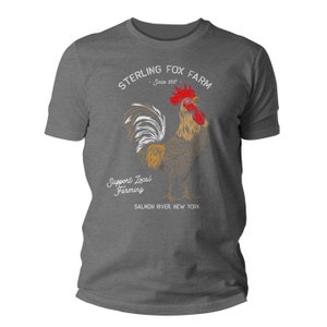 Peut inclure: Un t-shirt gris fonc&eacute; avec un graphique blanc d'un coq avec le texte "Sterling Fox Farm - Since 2017" et "Support Local Farming - Salmon River, New York".
