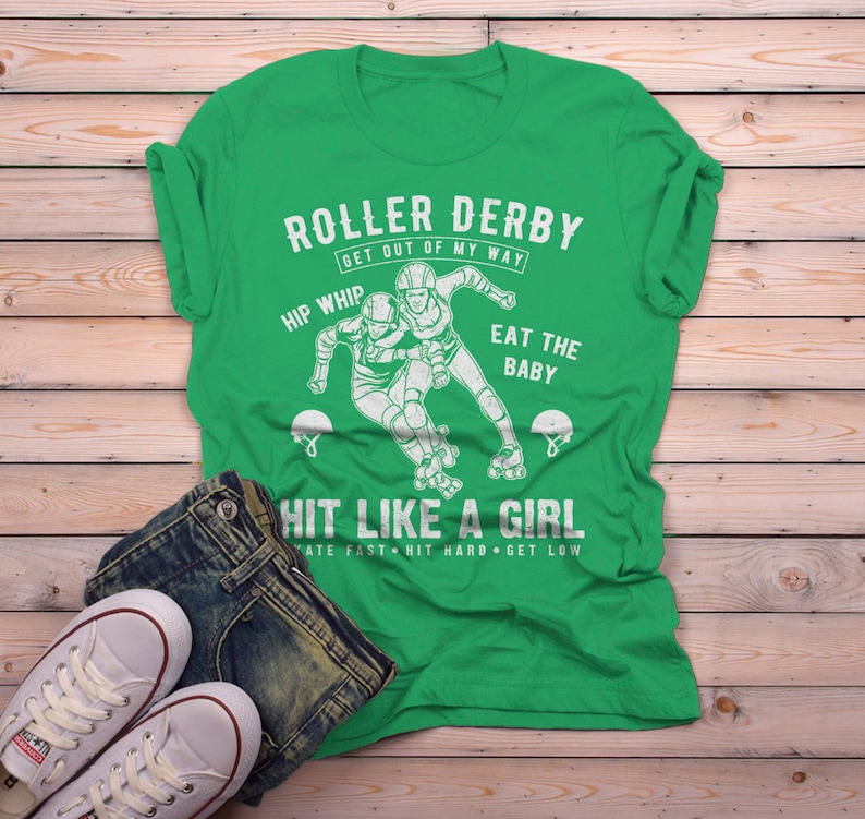 May include: Green t-shirt with a white graphic of two roller derby players. The text reads "Roller Derby Get Out of My Way Hip Whip Eat the Baby Hit Like a Girl Skate Fast Hit Hard Get Low".
