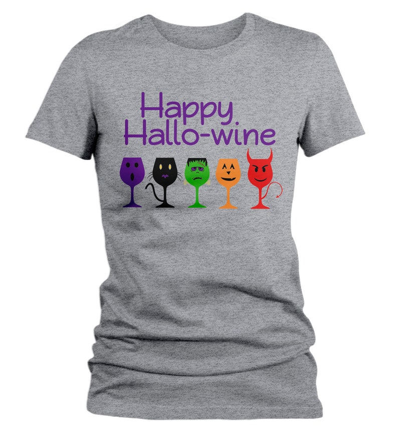 K&ouml;nnte beinhalten: Graues T-Shirt mit dem Text "Happy Hallo-wine" in Lila. F&uuml;nf Weingl&auml;ser mit verschiedenen Halloween-Charaktergesichtern sind unter dem Text aufgereiht.