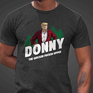 May include: Dark gray t-shirt with the word "DONNY" in large white letters, and the phrase "THE QUICKER FUCKER UPPER" below. The shirt features an illustration of a man in a red plaid jacket and white shirt, with green trees in the background.
