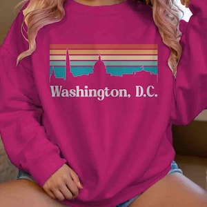 May include: A pink sweatshirt with a retro-style graphic of the Washington, D.C. skyline and the text "Washington, D.C."
