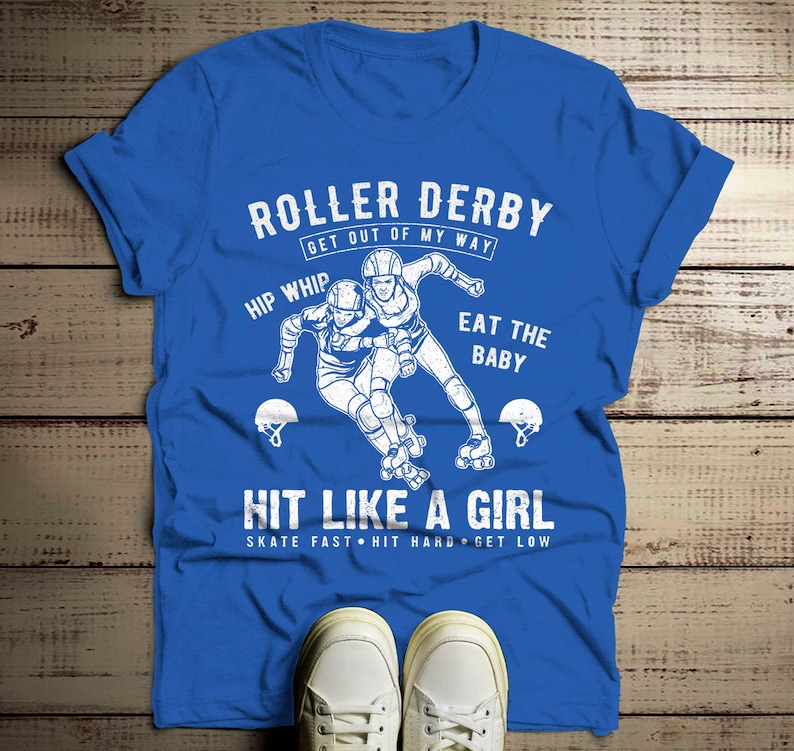 May include: Blue t-shirt with a white graphic of two roller derby skaters. The text on the shirt reads "Roller Derby Get Out Of My Way Hip Whip Eat The Baby Hit Like A Girl Skate Fast Hit Hard Get Low".