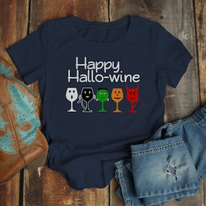 K&ouml;nnte beinhalten: Ein marineblaues T-Shirt mit dem Text "Happy Hallo-wine" und einer Reihe von f&uuml;nf Weingl&auml;sern mit verschiedenen Halloween-Charaktergesichtern.