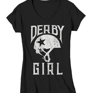 May include: Black v-neck t-shirt with a white graphic of a roller derby helmet with a star and the text "Derby Girl".