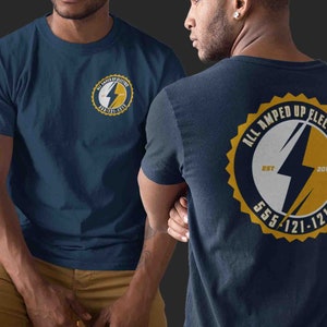 May include: A navy blue t-shirt with a yellow and white logo on the back. The logo is a circle with the text "All Amped Up Electric" and a lightning bolt inside. The text "Est 2015" and "555-121-1212" are also on the logo.