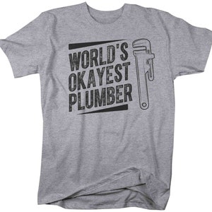 May include: Gray t-shirt with black text that reads "World's Okayest Plumber" and a black and white illustration of a wrench.