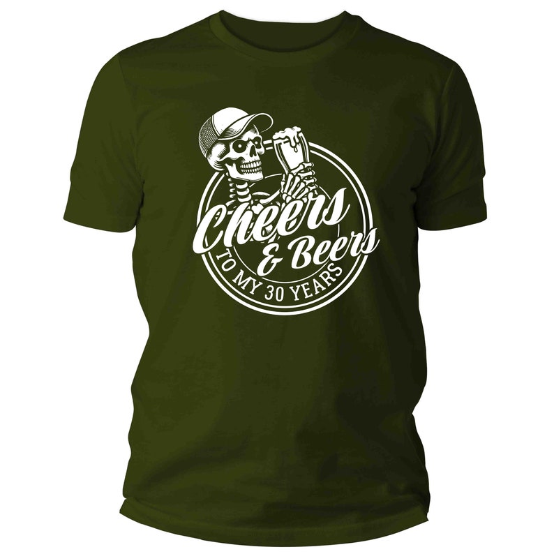 May include: Dark olive green t-shirt with a white graphic. The graphic shows a skeleton in a cap, holding a beer, and the text "Cheers & Beers To My 30 Years" in a circular design. A casual wear item.