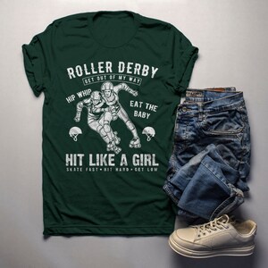 May include: Green t-shirt with a white graphic of two roller derby players. The text on the shirt reads "Roller Derby Get Out Of My Way Hip Whip Eat The Baby Hit Like A Girl Skate Fast Hit Hard Get Low".