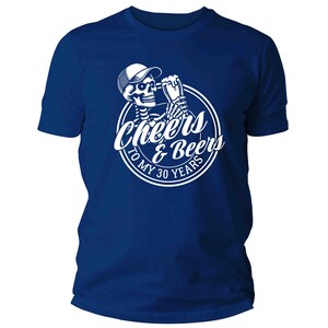 May include: A royal blue t-shirt with a white graphic of a skeleton in a cap, toasting with a beer. The graphic is in a white circle with the text "Cheers & Beers To My 30 Years".