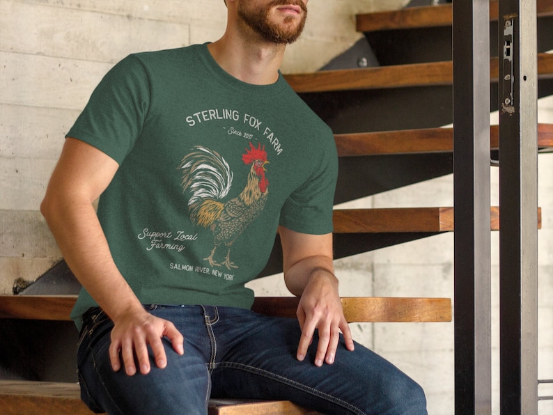 Peut inclure: Un t-shirt vert avec une illustration de coq et le texte "Sterling Fox Farm Since 2017 Support Local Farming Salmon River New York".