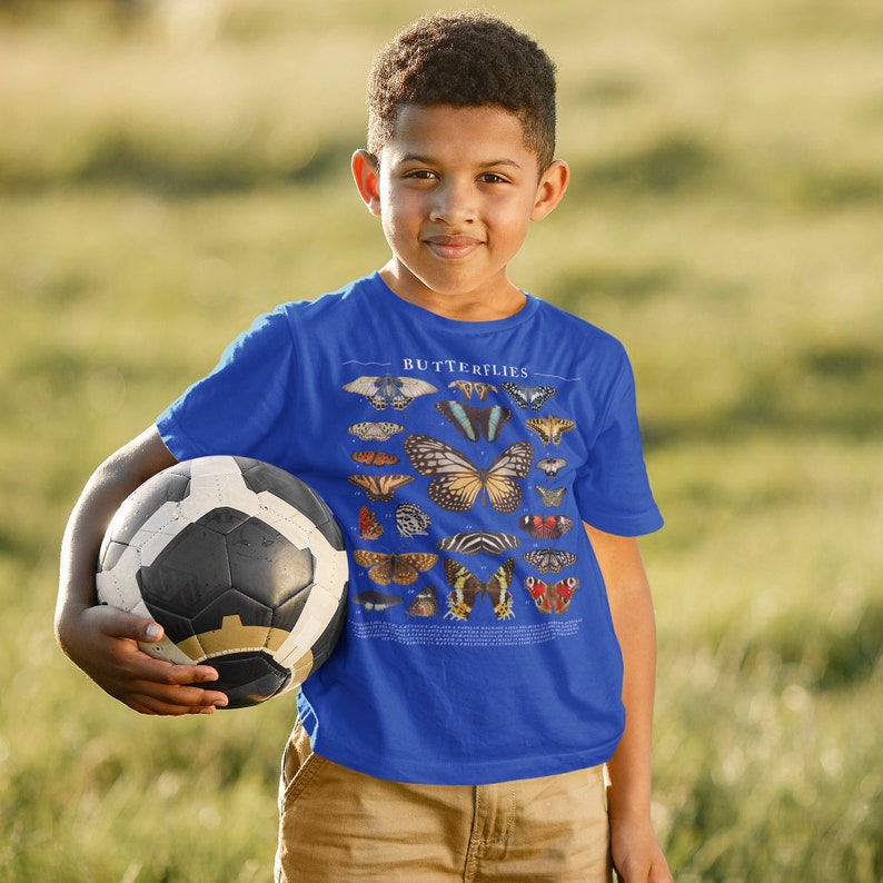 May include: A young person wearing a royal blue t-shirt with a graphic of various butterflies and the word "Butterflies" printed on the front. The person is holding a black and white soccer ball.