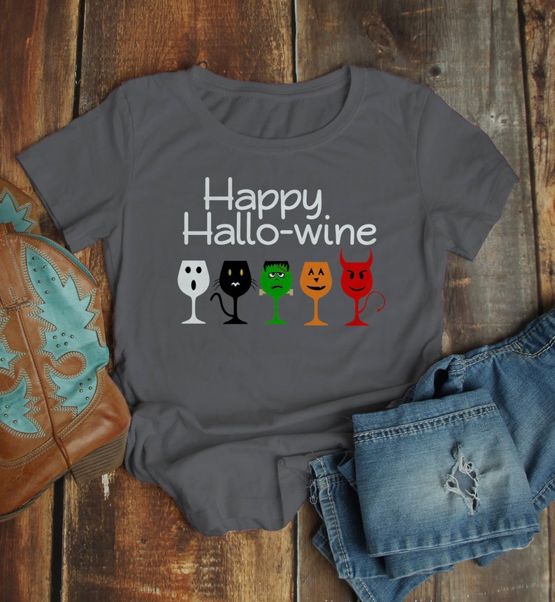 K&ouml;nnte beinhalten: Ein dunkelgraues T-Shirt mit dem Text "Happy Hallo-wine" und einer Reihe von f&uuml;nf Weingl&auml;sern mit Halloween-Charaktergesichtern. Die Gl&auml;ser sind ein Geist, eine schwarze Katze, Frankenstein, ein K&uuml;rbis und ein Teufel.