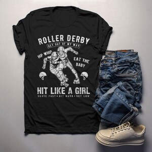 May include: Black t-shirt with a white graphic of two roller derby skaters. The text on the shirt reads "Roller Derby Get Out Of My Way Hip Whip Eat The Baby Hit Like A Girl Skate Fast Hit Hard Get Low".