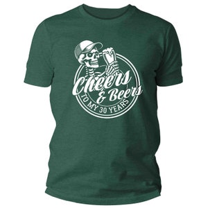 May include: Dark green t-shirt featuring a white graphic of a skeleton in a cap, toasting with a beer, and the text "Cheers & Beers To My 30 Years". The shirt has a crew neck.