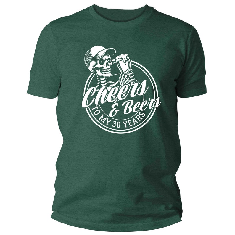 May include: Dark green t-shirt featuring a white graphic of a skeleton in a cap, toasting with a beer, and the text "Cheers & Beers To My 30 Years". The shirt has a crew neck.
