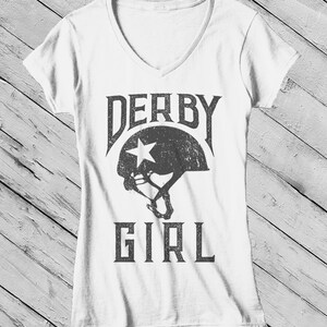 May include: White V-neck t-shirt with a distressed gray graphic of a roller derby helmet and the text "DERBY GIRL".