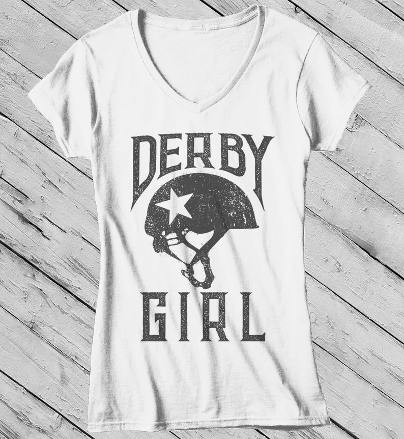 May include: White V-neck t-shirt with a distressed gray graphic of a roller derby helmet and the text "DERBY GIRL".