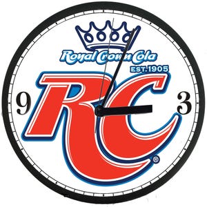 May include: Round wall clock featuring the Royal Crown Cola logo in red and blue on a white background. The clock has a black bezel and hands, with the numbers 9 and 3 visible. The text "Royal Crown Cola EST. 1905" is also displayed.