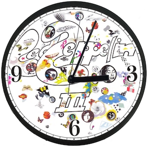 May include: A round wall clock with a black frame and a white face. The clock face features the band name "Led Zeppelin" in a stylized font, along with various colorful illustrations and the number 3, 6, and 9. The clock hands are black.