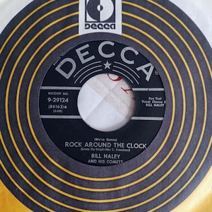 May include: A vintage 45 RPM vinyl record for the song "Rock Around the Clock" by Bill Haley and His Comets. The record label is black with white text and a Decca Records logo. The record is in a yellow and black sleeve.