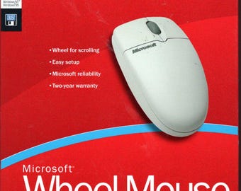 Op de afbeelding: Een witte Microsoft Wheel Mouse op een rode achtergrond. De doos heeft het Microsoft-logo en de tekst "Simply the Better Value". Extra tekst is onder meer "Wheel for scrolling", "Easy setup" en "Two-year warranty".
