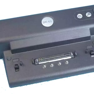 May include: A black Dell laptop docking station with a power button, a connector for a laptop, and a Dell logo.