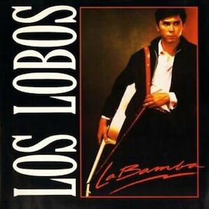 Könnte beinhalten: Ein schwarzes und weißes Albumcover mit dem Text "Los Lobos" in weißen Buchstaben. Das Albumcover zeigt einen Mann in einer schwarzen Jacke, der eine Gitarre hält. Der Text "La Bamba" ist in roter Kursivschrift in der unteren rechten Ecke des Albumcovers geschrieben.