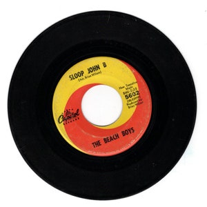 May include: A black vinyl record with a yellow and red label. The label features the text "SLOOP JOHN B (Arr. Brian Wilson)" and "THE BEACH BOYS". The record number "5602" is printed on the label.