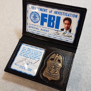 Könnte beinhalten: Schwarzer FBI-Ausweishalter aus Leder mit einem goldfarbenen Abzeichen und Ausweisen. Auf dem Abzeichen steht "Justice Department Federal Bureau of Investigation". Ein Ausweis zeigt ein Foto und den Namen "Fox Mulder".