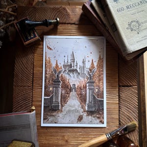 May include: Watercolor print of a castle with tall spires, set amidst a forest with autumn foliage. The artwork features a long pathway leading to the castle, flanked by statues. The print is framed and rests on a wooden surface, surrounded by books and art supplies.
