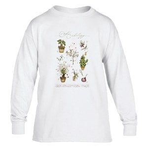 May include: A white long-sleeve shirt featuring a central graphic titled Herbology. The illustration displays various botanical drawings of plants in pots, bulbs, and stems with numbered labels and small text descriptions arranged in a grid.