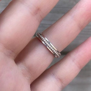 Könnte beinhalten: Ein silberner Ring mit einem Perlenmuster. Der Ring wird an einem Finger getragen.