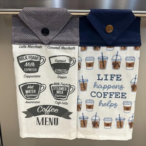 Könnte beinhalten: Zwei weiße Küchentücher mit Kaffee-Motiven in Schwarz und Grau. Das linke Handtuch zeigt eine Kaffeekarte mit verschiedenen Kaffeesorten. Das rechte Handtuch hat ein blaues und weißes Design mit dem Text "Das Leben passiert, Kaffee hilft".