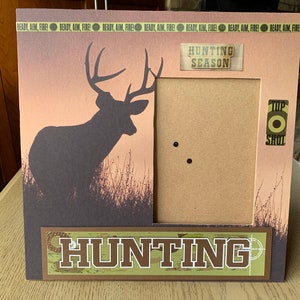 Könnte beinhalten: Ein brauner Bilderrahmen mit einer Silhouette eines Hirsches im Hintergrund. Der Rahmen hat einen Ausschnitt für ein Foto und einen braunen Papierhintergrund. Der Text "Hunting Season" befindet sich oben am Rahmen und der Text "Hunting" unten am Rahmen. Der Text "Top Shot" befindet sich rechts am Rahmen.
