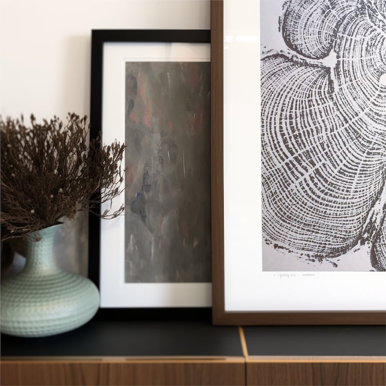 May include: Two framed pictures hanging on a wall. The picture on the left has a brown and gray abstract design. The picture on the right has a black and white image of tree rings.