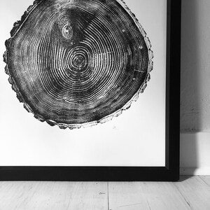 May include: Black and white print of a tree trunk cross-section, showing the rings of growth. The print is framed in a black frame and is hanging on a white wall.