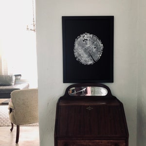 May include: A black framed print of a tree trunk cross section with a white background. The print is hanging on a white wall above a dark wood desk with a mirror.