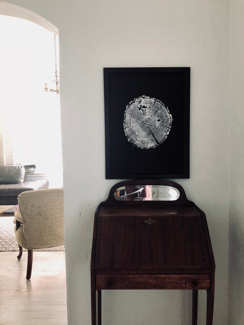 May include: A black framed print of a tree trunk cross section with a white background. The print is hanging on a white wall above a dark wood desk with a mirror.