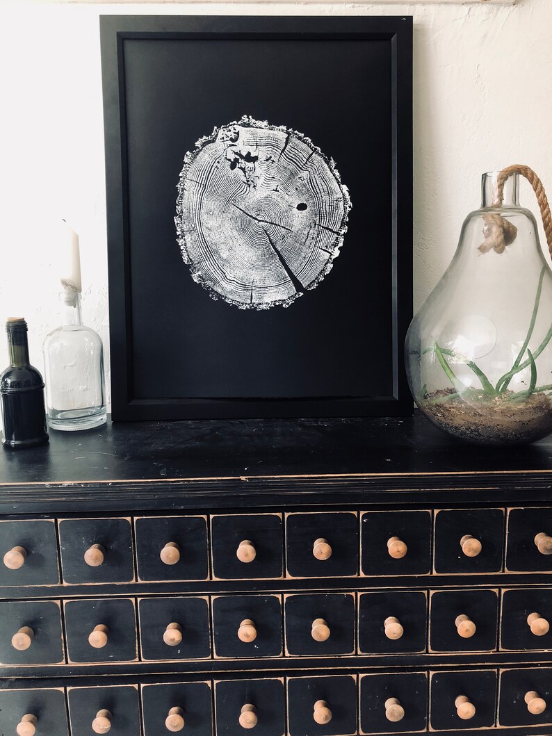 May include: A black framed print of a white tree ring on a black background. The print is sitting on a black dresser with multiple drawers. The dresser has wooden knobs.