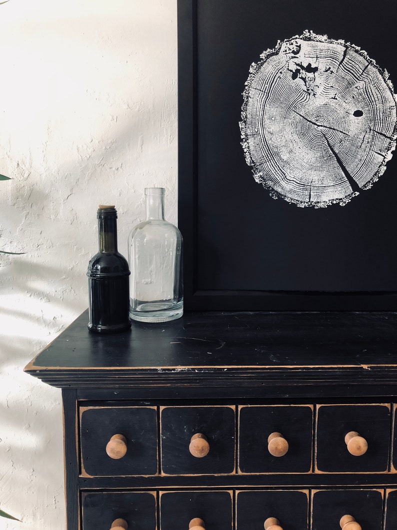 May include: A black dresser with eight drawers and wooden knobs. The dresser has a distressed finish and is topped with a framed black and white print of a tree ring. Two glass bottles are on the dresser.